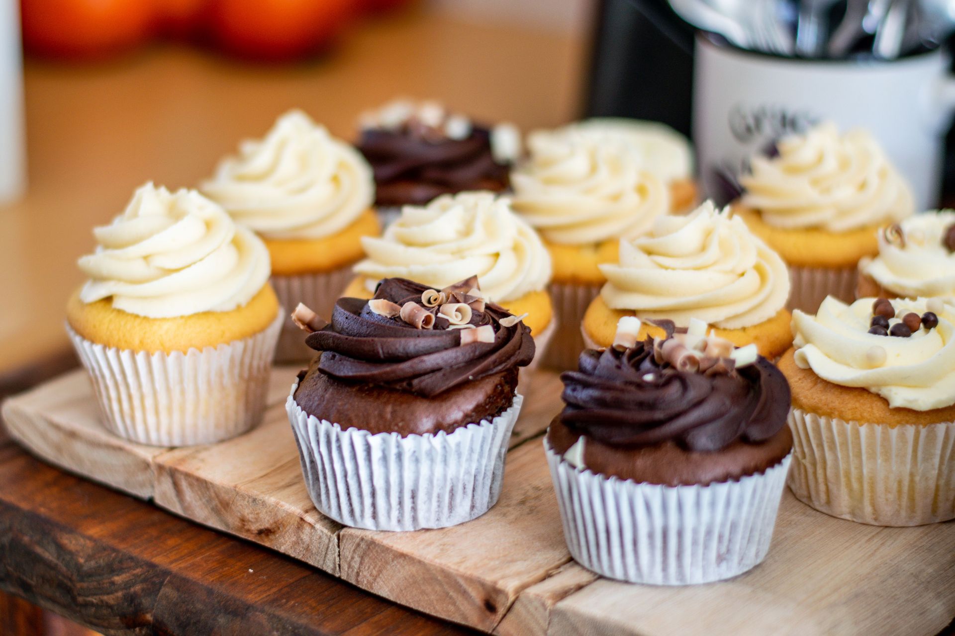 A variety of chocolate and vanilla cupcakes with creamy frosting arranged on a rustic wooden board.